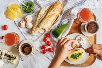 Overhead shot of a delicious breakfast flatlay featuring fresh ingredients and coffee on a white tablecloth.